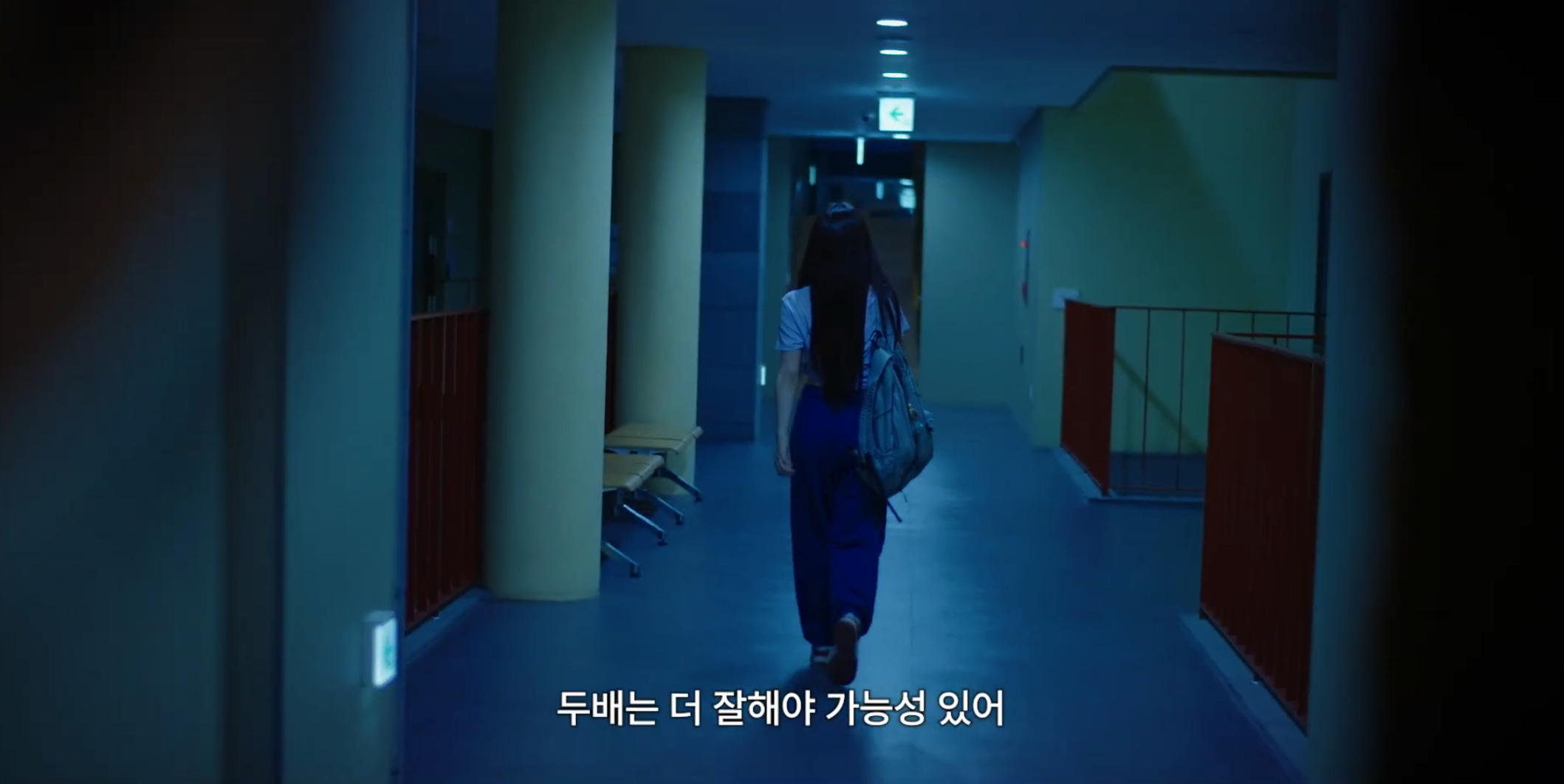 A character walks down a blue-lit corridor carrying a grey bag over one shoulder